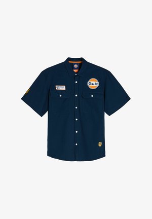 Granatowa koszula z krótkim rękawem wykonana z bawełny, z dwiema kieszeniami z przodu, logo Gulf i żółtymi akcentami na rękawie oraz dolnym brzegu.