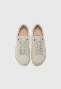Beige sneakers med en myk tekstiloverdel, rund tå og flate lisser. Lysebrun gummisåle med subtil merking på tungen.