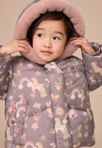 Manteau matelassé gris avec motifs pastel de licornes et fleurs, capuche en fausse fourrure rose douce, et fermeture devant avec une poche sur le côté gauche.