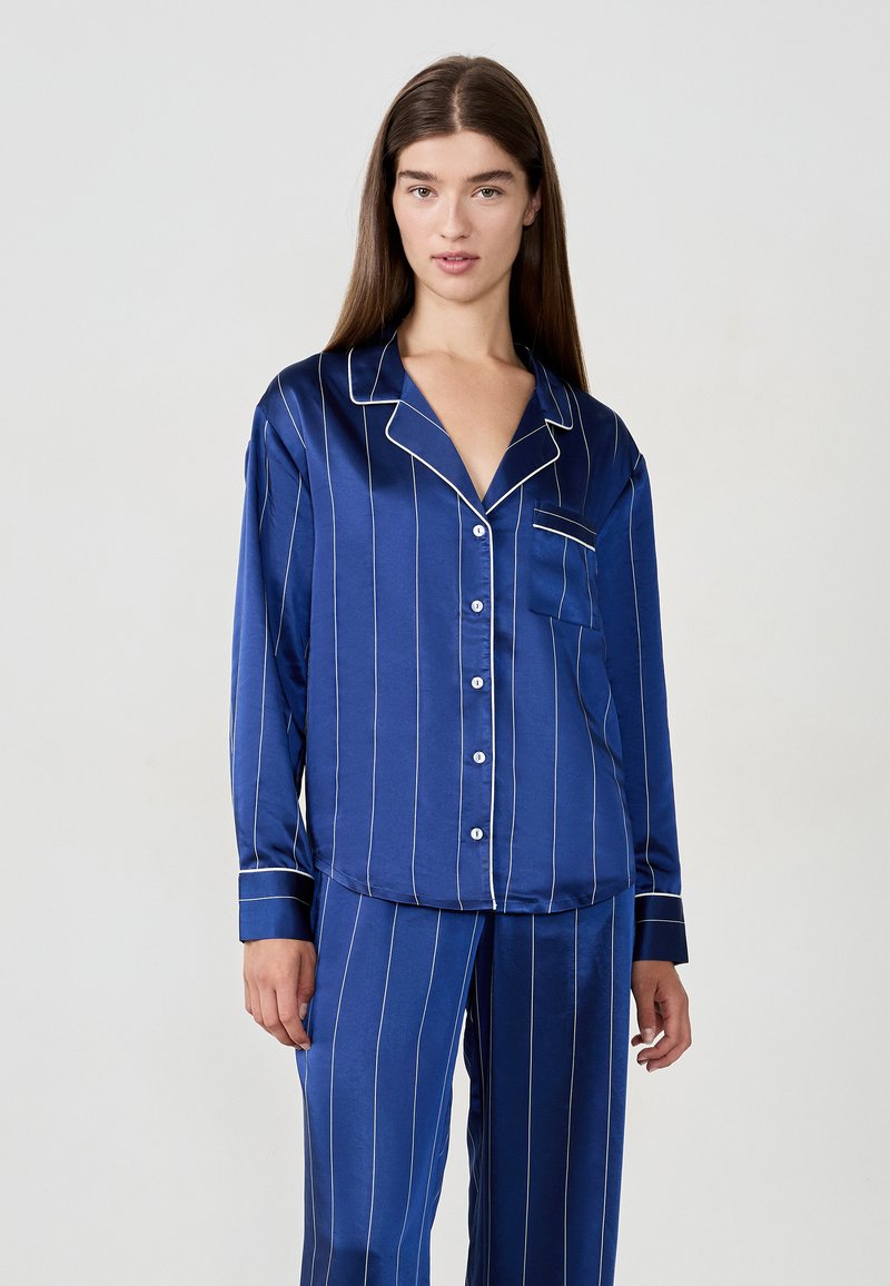 Mörkblå satin pyjamasuppsättning med vita vertikala ränder. Innehåller en skjorta med krage och knapplist, samt matchande byxor.