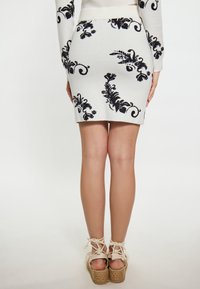 Fustă tricotată albă cu modele florale negre, design ajustat, cu o deschidere la tiv; purtată cu sandale espadrile bej cu legături la glezne.