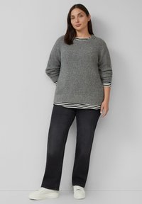 Grijze gebreide trui met een geribbelde textuur, met zwart-witte gestreepte accenten bij de boorden en een gelaagde look over donkere jeans.