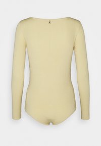 Pitkähihainen bodysuit pehmeästä, ribatusta kankaasta. Vaalea keltainen väri, pyöreä kaula-aukko ja kultainen vetoketj yksityiskohta takana.