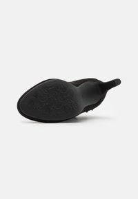Scarpa in suede nera con punta affilata e suola liscia, caratterizzata da un motivo floreale in rilievo. Il tacco è stretto e presenta un'etichetta in tessuto.