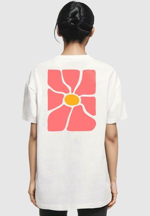 Weißes Baumwoll-T-Shirt mit einem großen pinken Blumenmotiv mit gelbem Zentrum auf dem Rücken, kurzen Ärmeln und lockerer Passform.