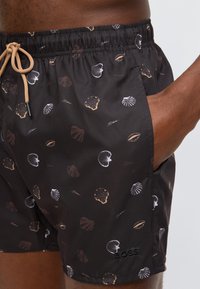 Μαύρα μαγιό σορτς με μπεζ και λευκά σχέδια κοχυλιών, ταμπά κορδόνι, πλαϊνή τσέπη και μαύρο κεντημένο λογότυπο "BOSS" στο δεξί πόδι.