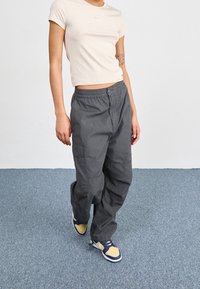 Grå cargo byxor med avslappnad passform, utrustade med elastisk midja, sidofickor och en mjuk textur, i kombination med en ljusbeige topp.