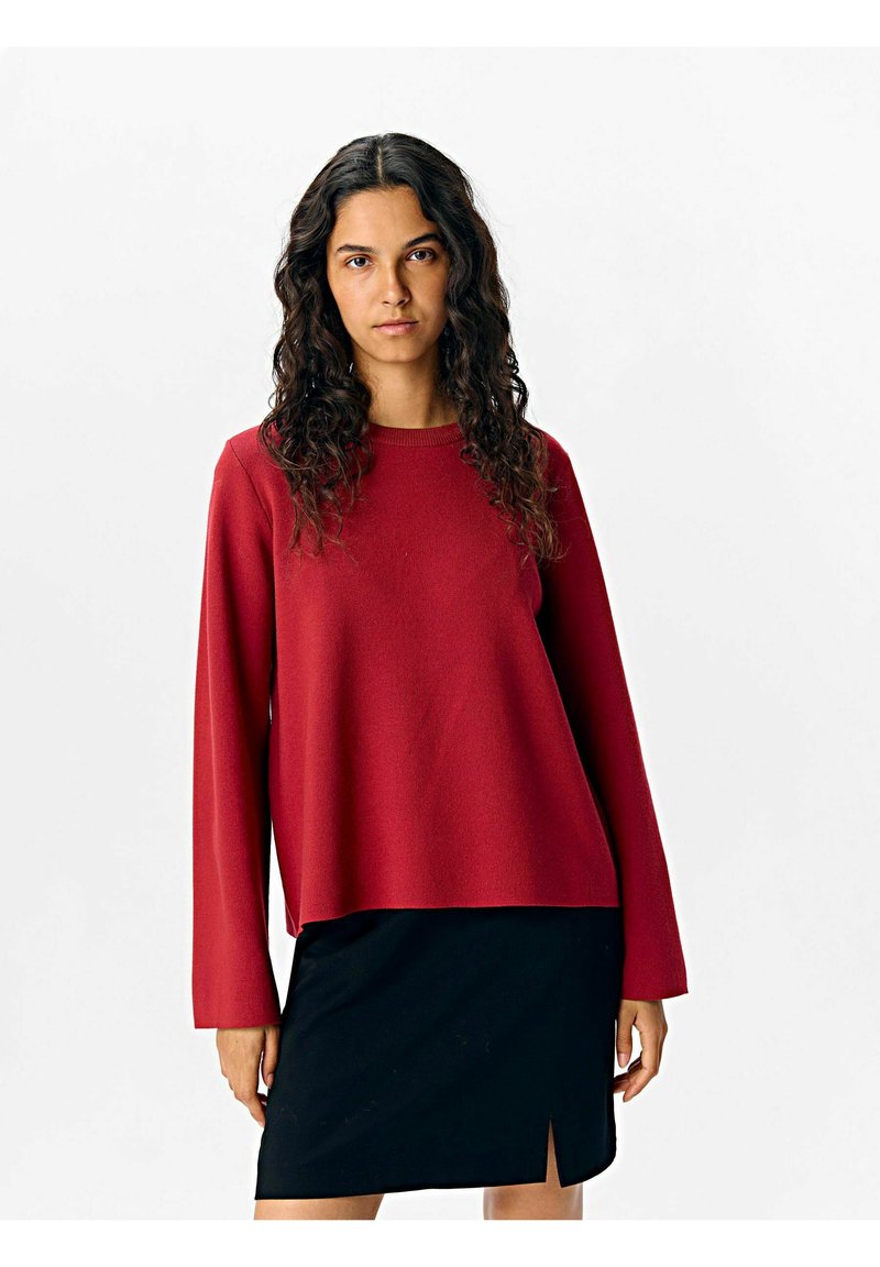 Pull rouge à manches longues en matière douce avec une coupe décontractée, dotée d'un col rond et d'un ourlet légèrement cropped. Assorti à une jupe noire.