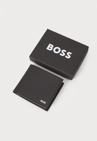 Zwart leren portemonnee plat naast een zwarte doos met het witte logo "BOSS". De portemonnee heeft strakke lijnen en minimale stiksels voor een elegante afwerking.