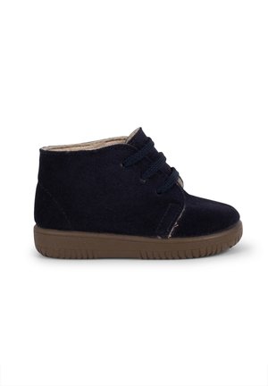 Stivaletti alla caviglia in suede blu navy con suola in gomma marrone, lacci anteriori, interno morbido e dettagli di cucitura minimali sui lati.
