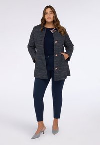 Marineblauer Tweed-Mantel mit roségoldenen Knöpfen, strukturiertem Stoff, seitlichen Taschen, kombiniert mit marineblauen Hosen und grauen spitzen Absatzschuhen.