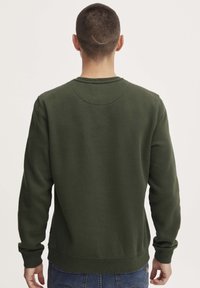 Donkergroen sweatshirt met een ronde hals, ribgebreide manchetten en zoom. Heeft een gladde textuur en een naaddetail langs de achterkant.