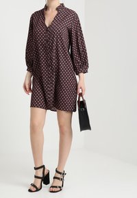 Short-sleeve, button-up dress in dark fabric with a geometric pattern. Worn with black ankle strap heels and a small handbag.