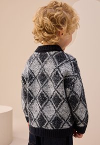 Suéter de punto para niños en gris y azul marino con un patrón de diamantes. Cuenta con un cuello y puños acanalados, tejido texturizado y un ajuste holgado.