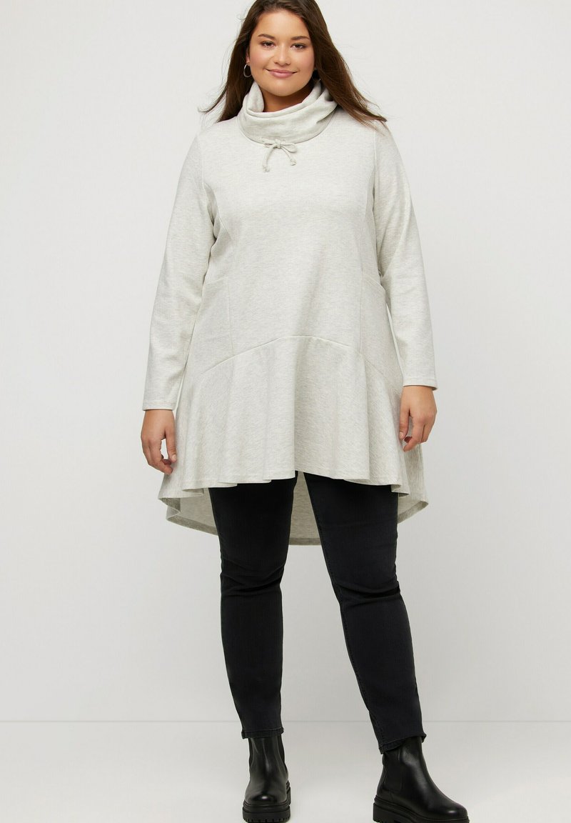 Túnica de manga larga gris claro con cuello de capucha, detalle de cordón, dobladillo acampanado y textura suave, combinada con pantalones ajustados negros y botas de tobillo.