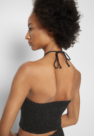 Top halter cropped preto com smocking texturizado, preso no pescoço com cordões finos, exibindo costas nuas e design minimalista.