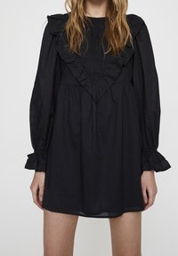 Robe noire avec un corsage smocké et un col à volants, dotée de manches longues avec des poignets à volants et une forme fluide en ligne A.