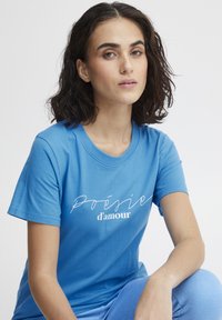 Modrá bavlněná tričko s krátkým rukávem s bílým nápisem "Poésie d'amour" na hrudi. Volný střih, měkká textura.