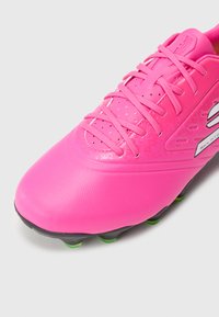 Rozā futbola kurpe ar strukturētu sintētisku augšdaļu, kas izceļas ar plānām šņorēm, perforācijām ventilācijai un melnu un zaļu zoli.