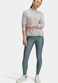 Grau Hoodie mit Kordelzug, kombiniert mit türkisfarbenen Leggings. Die Leggings haben eine glatte Textur und ein kleines Logo. Weiße Sportschuhe runden das Outfit ab.