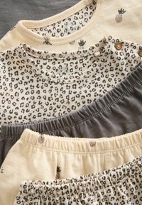 Sæt af tøj med en leopardprint top i beige og grå, med elastiske taljebånd og ananasdetaljer på bukserne.