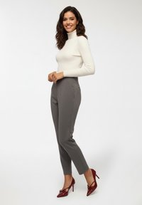 Biały prążkowany sweter z golfem, szare dopasowane spodnie z zakładkami i bordowe czółenka na szpilce z kokardkami.