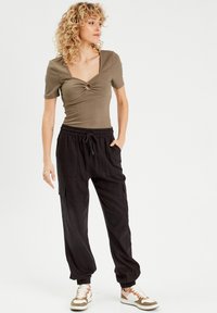 Haut de couleur olive à côtes, avec un décolleté carré et un détail en noué, associé à un pantalon cargo noir ample avec poches latérales et poignets resserrés.