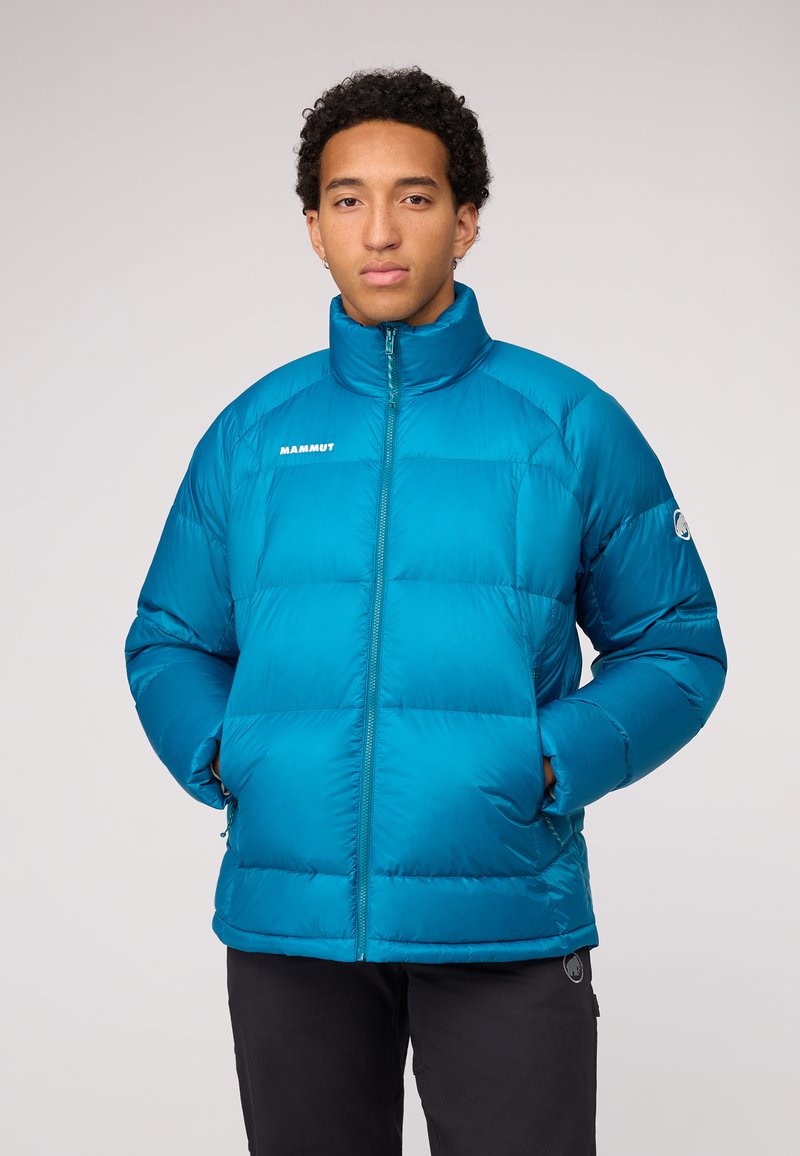 Türkisfarbene Pufferjacke mit hohem Kragen, Reißverschluss und Logo auf der Brust. Sie hat eine boxy Form und eine weiche, gesteppten Textur.
