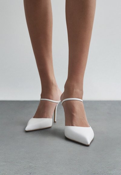 Bílé mule s vysokým podpatkem a špičatou špičkou, se průhledným páskem a jemnou texturou na koženém svršku. Hladký, elegantní vzhled.