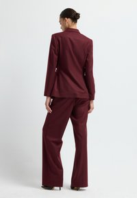 Completo due pezzi bordeaux composto da un blazer strutturato e pantaloni a gamba larga, realizzato in un tessuto morbido con una vestibilità su misura e linee pulite.