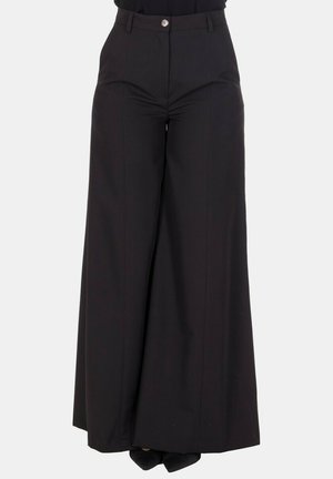 Pantaloni neri a vita alta e gamba larga con bottone e zip frontali, indossati con scarpe nere a punta su sfondo uniforme.