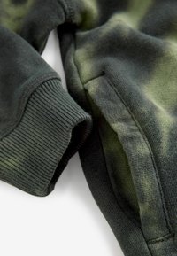 Dunkelgrünes Sweatshirt mit geripptem Bündchen und einem Batikmuster. Strukturierter Stoff mit glatter Oberfläche, ausgestattet mit einem Seitentaschen-Detail.