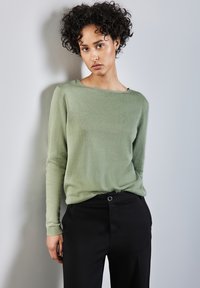 Hellgrüner, langärmeliger Strickpullover mit U-Boot-Ausschnitt, kombiniert mit schwarzen, hoch taillierten Hosen mit Knopfdetail.