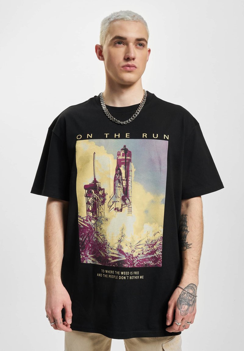 Sort bomuld t-shirt med et farverigt grafik af en raketopsendelse, text nederst, og afslappet pasform. Modellen bærer en sølvkæde.