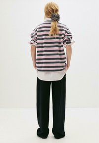 Stripet oversized pullover med grå og lyserøde striber, parret med en hvid tekstureret skjorte under og brede sorte bukser.