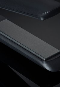 Zwarte stijltang met een gestructureerde grijze plaat. Glad, afgeronde randen aan de bovenkant, metalen hardware en een minimalistisch ontwerp.