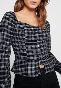 Chemise à carreaux noir et blanc à boutons avec des manches longues, décolleté carré, taille peplum et texture de tissu douce.