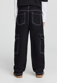 Pantaloni cargo neri con cuciture bianche, dotati di due tasche laterali e due tasche posteriori. Fit morbido e polsini affusolati alle caviglie.