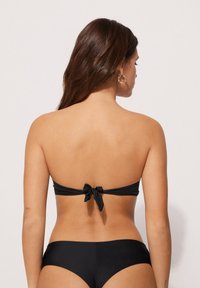Zwarte bikini met een bandeau top en een strik achterop, en bijpassende onderkant. Glad textuur, eenvoudig ontwerp, geschikt voor zwemmen of zonnebaden.