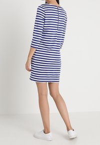 Blauwe en witte gestreepte jurk met een rechte snit, driekwart mouwen en een ritssluiting op de rug, gecombineerd met witte sneakers.