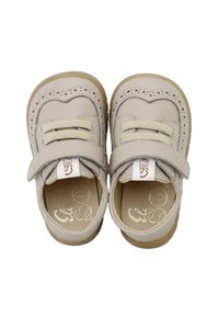 Zapatos de cuero color beige claro con puntera redondeada, perforaciones decorativas y una correa de velcro, con suela de goma y forro interior suave.