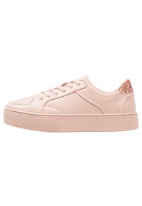 Ljust rosa sneaker med texturerat läder, platt sula och en glitterdetalj på hälen. Har rundad tå och snörning för att fästa.