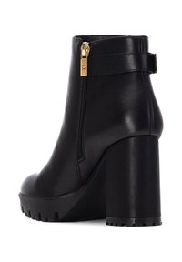 Stivale alla caviglia in pelle nera con tacco alto e chunky, zip laterale e cinturino decorativo con hardware dorato. Suola testurizzata per la presa.