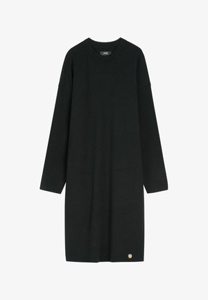 Czarna dzianinowa sukienka z długim rękawem, z okrągłym dekoltem i małym złotym okrągłym emblematem przy Krawędzi, prezentowana na jednolitym białym tle.