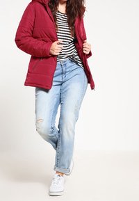 Red padded jacket with a hood, striped black and white shirt, light blue distressed jeans, and white sneakers. Casual outfit arrangement.