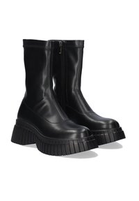 Botas de tobillo de cuero sintético negro con una suela de plataforma gruesa y texturizada, y cremallera lateral. La parte superior presenta superficies lisas y brillantes, con acentos de costura.