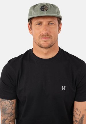 T-shirt noir avec un petit logo blanc sur la poitrine gauche, associé à une casquette vert clair portant un logo rond foncé à l'avant.