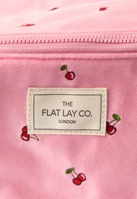 Roze stoffen etui met geborduurde kersen en een label met de tekst "THE FLAT LAY CO. LONDON." Ritssluiting aan de bovenkant. Zachte textuur.