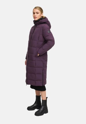 Polstret lang lilla frakke med hætte, der har lynlås foran, sidelommer og en bungee-snøre til justering. Båret over en sort sweater og støvler.