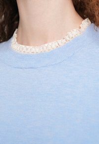 Ανοιχτό μπλε πουλόβερ με ριμπ στρογγυλή λαιμόκοψη, διακοσμημένο με λευκή δαντελένια τρέσα. Μαλακή υφή, μεσαίου πάχους, με ελάχιστες ορατές ραφές.